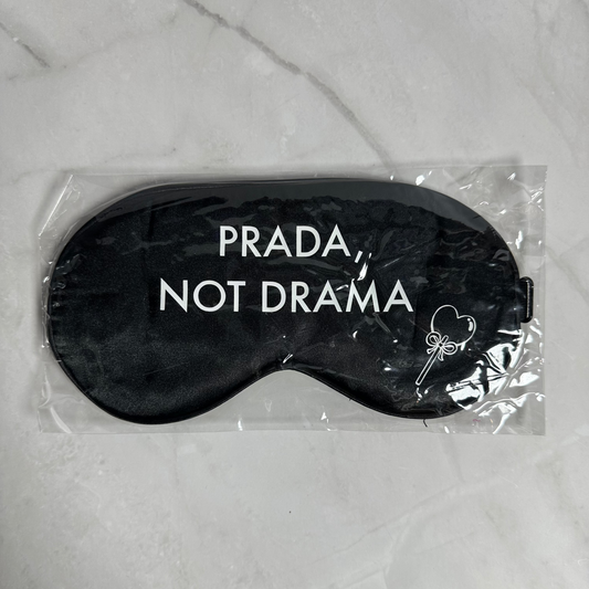 Black sleep mask with 'Prada Not Drama' text in clear packaging on a marble surface